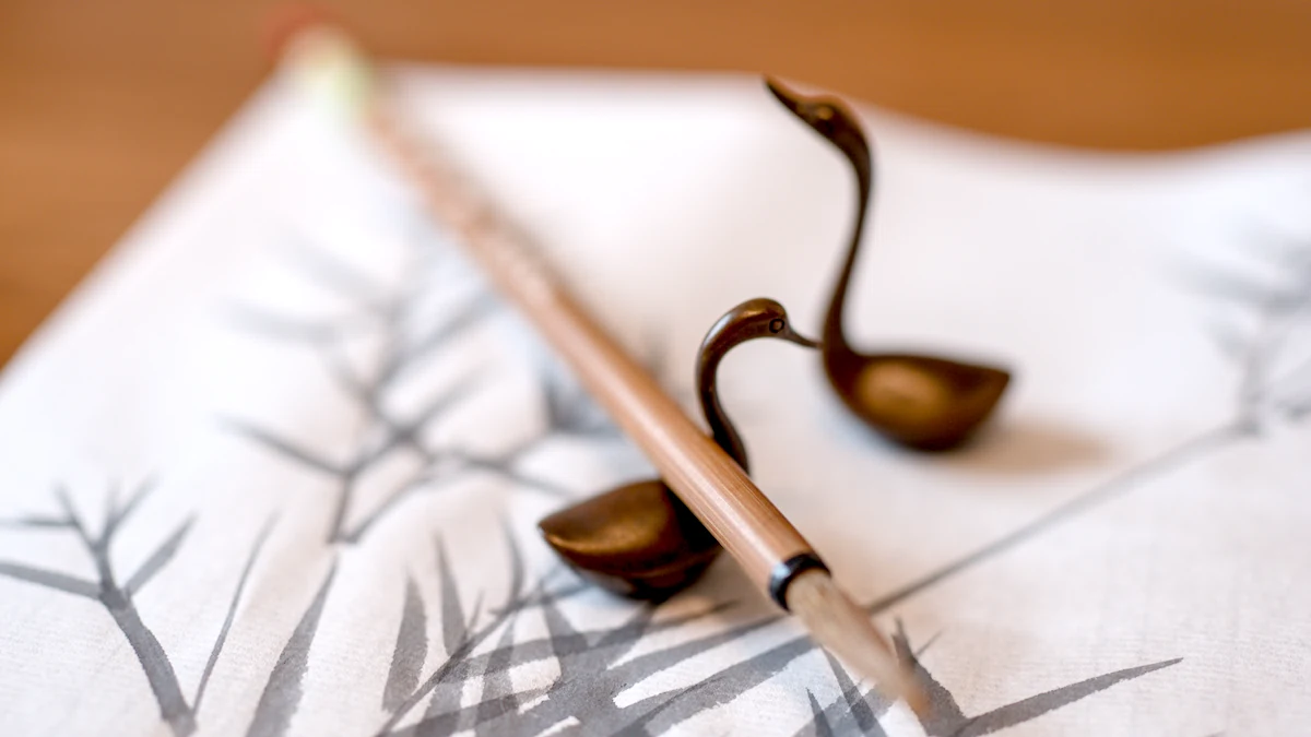 Two brushes resting on a brass goose-shaped brush rest over a sheet of painted bamboo